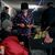 Ein Polizist in Awdijiwka beschenkt Menschen mit Mandarinen und Äpfeln in der Vorweihnachtszeit in einem als Bunker genutzten Keller eines Wohnhauses. - Foto: Libkos/AP/dpa
